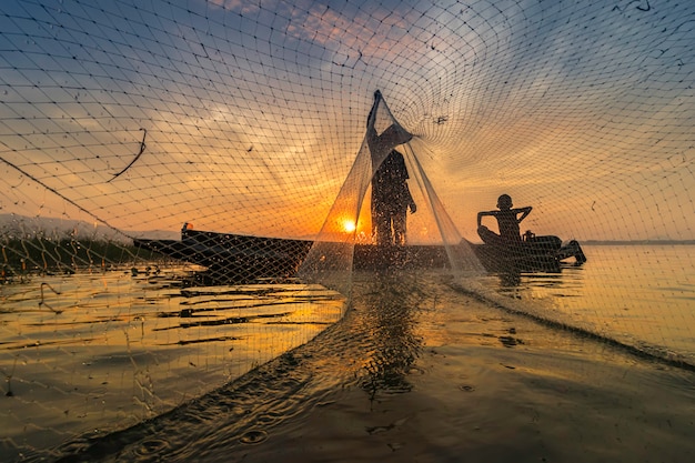 La imagen es silueta. Pescadores Casting salen a pescar temprano en la mañana con botes de madera.