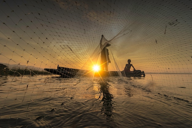 La imagen es silueta. Los pescadores lanzan a pescar temprano en la mañana con botes de madera, linternas viejas y redes. Concepto de estilo de vida de los pescadores.