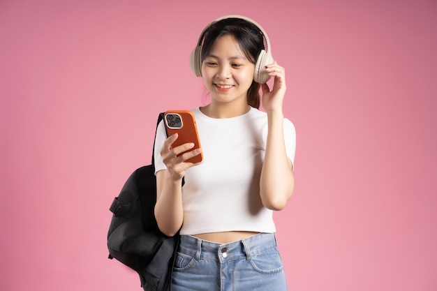 Imagen de una estudiante asiática sosteniendo un teléfono y aislada en un fondo rosa