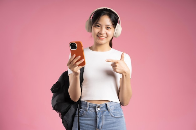 Imagen de una estudiante asiática sosteniendo un teléfono y aislada en un fondo rosa