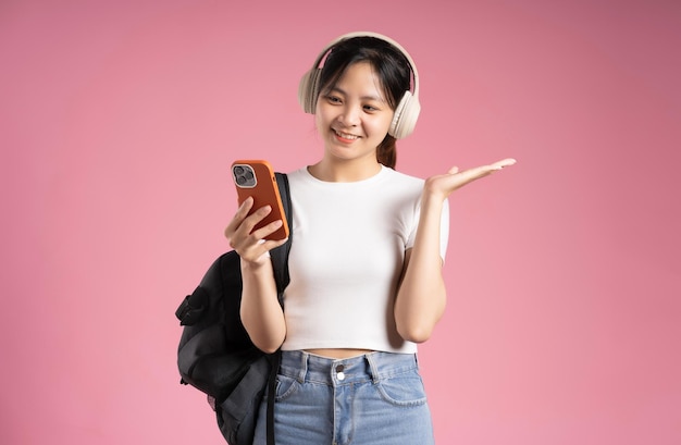 Imagen de una estudiante asiática sosteniendo un teléfono y aislada en un fondo rosa