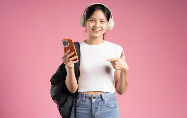 Imagen de una estudiante asiática sosteniendo un teléfono y aislada en un fondo rosa