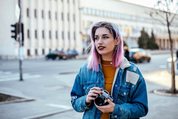 Imagen del estudiante o del fotógrafo hermoso con el pelo rosado en la calle de la ciudad.