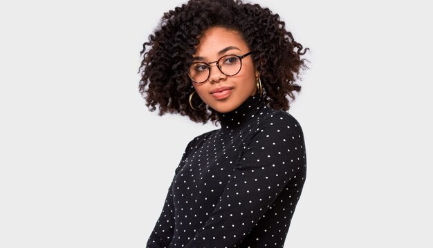 Imagen de estudio de una bonita joven afroamericana que viste ropa informal y anteojos Mujer afro con blusa negra posando sobre una pared blanca Concepto de personas y emociones