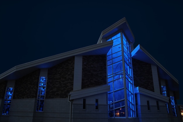 Imagen del exterior de la capilla con ventanas grandes iluminado en azul por la noche