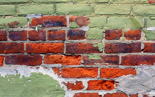 Imagen de la fachada pintada de verde se despega para mostrar un ladrillo rojo brillante debajo del fondo