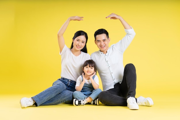 Imagen de una familia asiática sentada feliz y aislada en un fondo amarillo