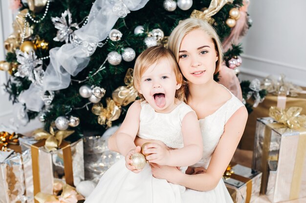 Imagen de familia caucásica de madre e hija en año nuevo con regalos alrededor del árbol de Navidad