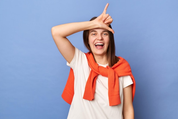 Imagen de una feliz y emocionada mujer caucásica con ropa de estilo informal aislada sobre fondo azul mostrando un gesto de shaka frente a su frente