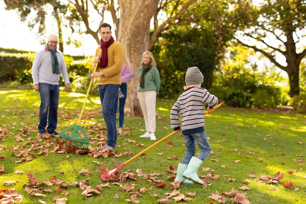 Imagen de una feliz familia caucásica de varias generaciones deslizando hojas en el jardín de otoño