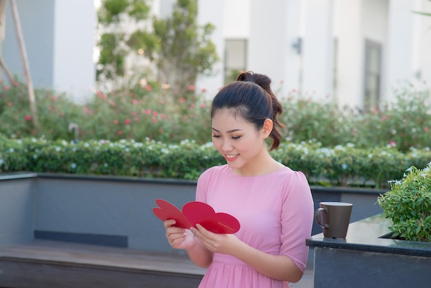 Imagen de feliz hermosa mujer leyendo postal romántica con gran corazón rojo, mujer atractiva tiene tarjeta de felicitación sensual, día de San Valentín, concepto de amor