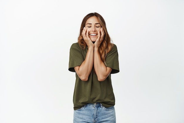 Imagen de feliz mujer de mediana edad regocijándose, sonriendo con los ojos cerrados, tocando el rostro natural limpio sin maquillaje