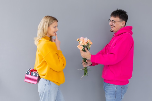 Imagen de una feliz pareja amorosa joven aislada sosteniendo una caja de regalo y flores