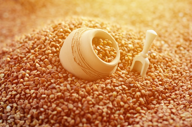 Imagen de fondo de una gran pila de trigo sarraceno, en medio de la cual se encuentra una jarra pequeña y una espátula de madera para los cereales
