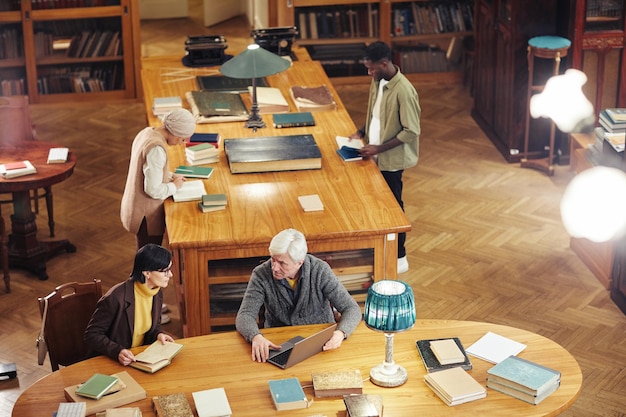 Imagen de fondo del interior de la biblioteca clásica con un grupo diverso de personas en el espacio de copia de la mesa de madera