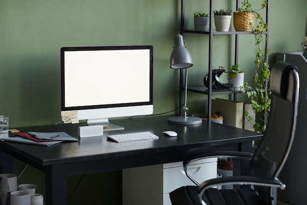 Imagen de fondo del lugar de trabajo de la oficina en casa con pantalla de computadora en blanco en el escritorio contra la copia de la pared verde