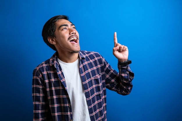 La imagen fotográfica de un joven estudiante asiático con camisa parecía feliz pensando y mirando hacia arriba, teniendo una buena idea. Retrato de medio cuerpo contra el fondo azul con espacio de copia