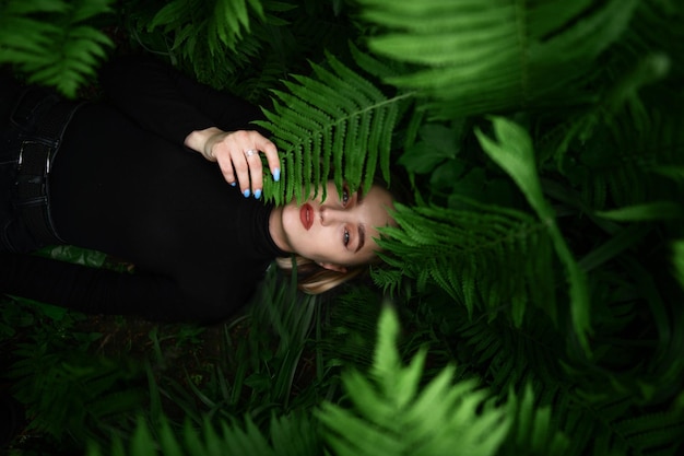 Imagen fresca natural de una mujer hermosa joven con el pelo rubio corto entre helechos en el suelo