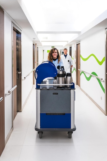 Imagen frontal de una enfermera alegre con un carrito de servicio de café listo para atender a los pacientes