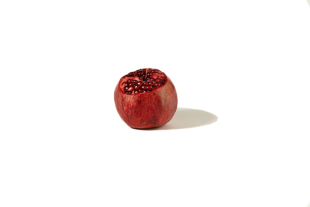 Imagen de una fruta de granada con una cáscara parcialmente cortada sobre un fondo blanco.