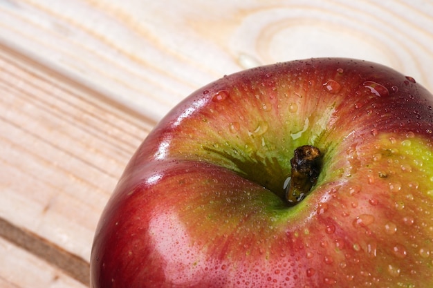 Imagen de fruta manzana dulce madura roja con gotas de rocío sobre un fondo de madera clara fotografía macro de cerca