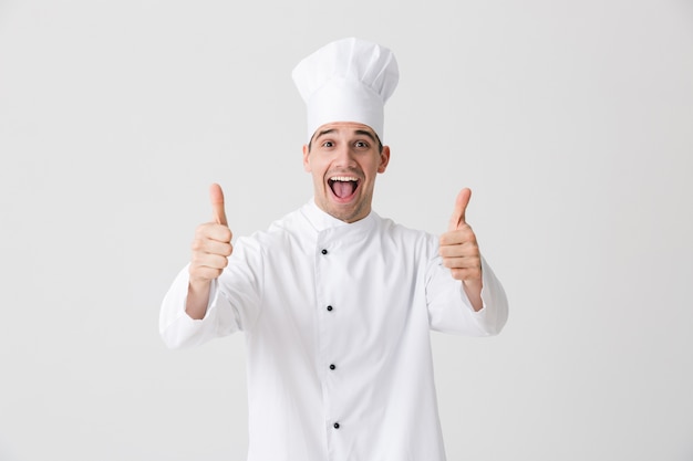 Imagen del guapo chef joven emocionado en el interior aislado sobre fondo de pared blanca mostrando los pulgares para arriba gesto.