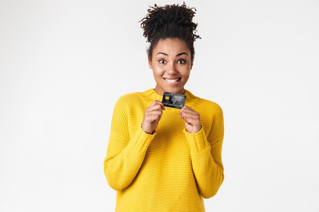 Foto imagen de una hermosa joven africana emocionada emocional feliz posando sobre una pared blanca con tarjeta de crédito.