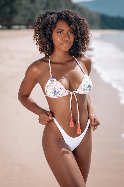 Imagen de la hermosa joven afroamericana en coloridos trajes de baño quedándose y posando en la cámara en la playa. Foto de Bayleigh Dayton - Miss Missouri 2017