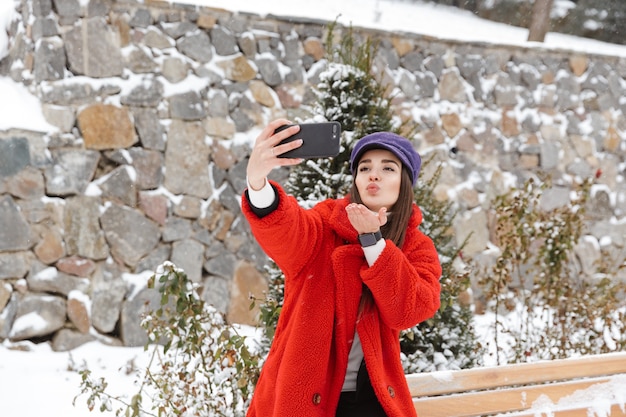 Imagen de la hermosa joven al aire libre en el bosque del parque de invierno de nieve tomar un selfie por teléfono móvil.