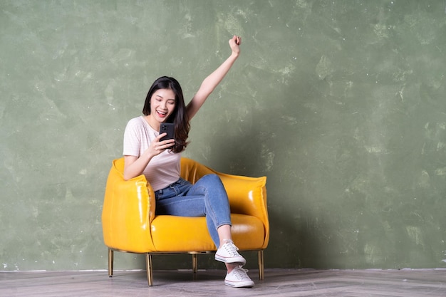 Imagen de una hermosa joven asiática sentada en un sillón amarillo