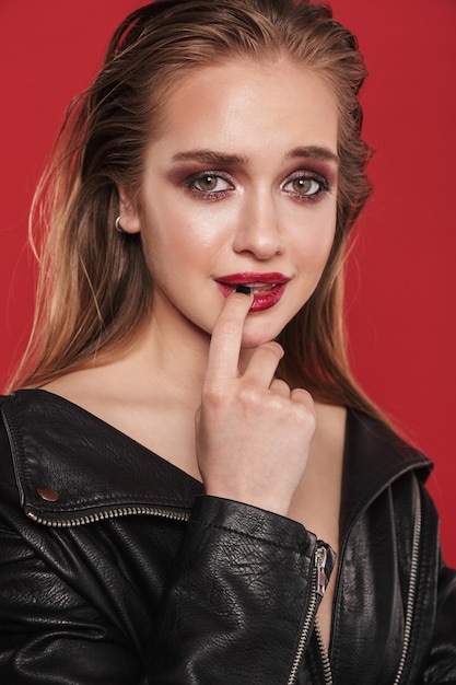 Imagen de una hermosa joven asombrosa con lápiz labial rojo maquillaje brillante posando sobre pared roja.