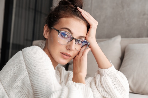 Foto imagen de la hermosa joven morena en anteojos descansando en el sofá en casa