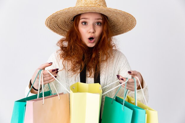 Imagen de una hermosa joven pelirroja emocionado emocionado linda chica posando aislada sobre fondo de pared blanca sosteniendo bolsas de la compra.