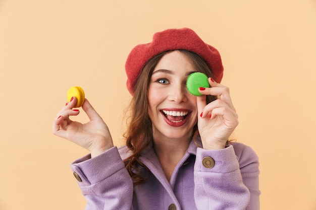 Imagen de hermosa mujer de 20 años con cabello largo sonriendo y sosteniendo galletas de macarrón, que se encuentran aisladas