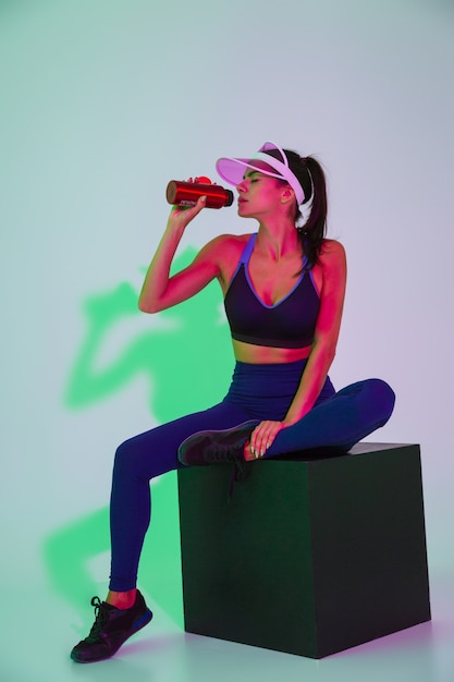 Imagen de una hermosa mujer de deportes bastante joven posando aislada con luces de flash LED en la tapa de agua potable.