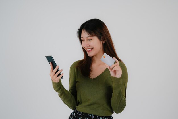 Imagen de una hermosa mujer joven y bonita posando aislada sobre un fondo de pared blanca usando un teléfono móvil con tarjeta de crédito