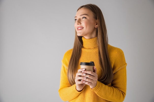 Imagen de una hermosa mujer joven feliz aislada sobre pared gris tomando café.