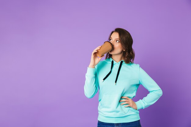 Imagen de una hermosa mujer joven posando aislada sobre la pared de la pared púrpura tomando café.