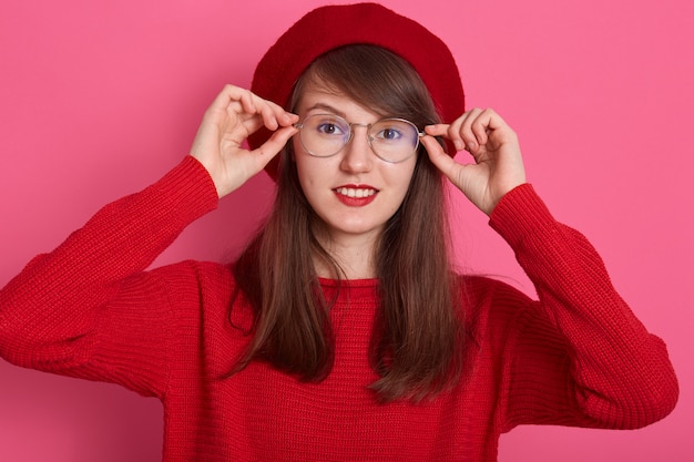 La imagen de una hermosa mujer de moda en estilo francés mantiene el dedo en sus gafas y tiene buen humor