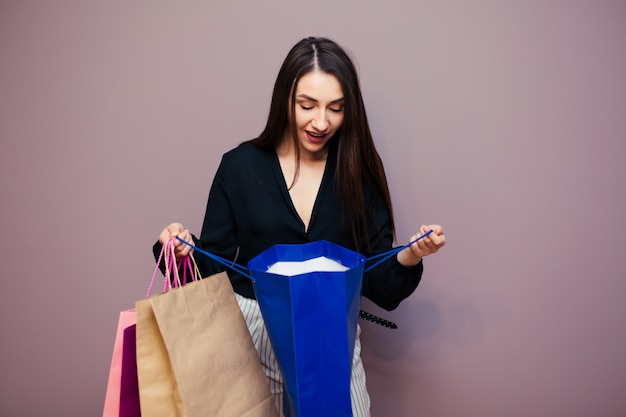 Imagen de una hermosa mujer rubia joven sorprendida posando aislada sobre la superficie de la pared de color rosa con bolsas de compras.