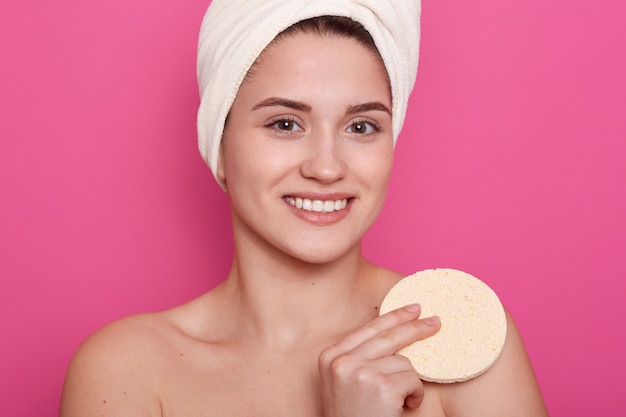 Imagen de la hermosa niña con una toalla blanca en la cabeza, está sonriendo y sosteniendo una esponja en la mano