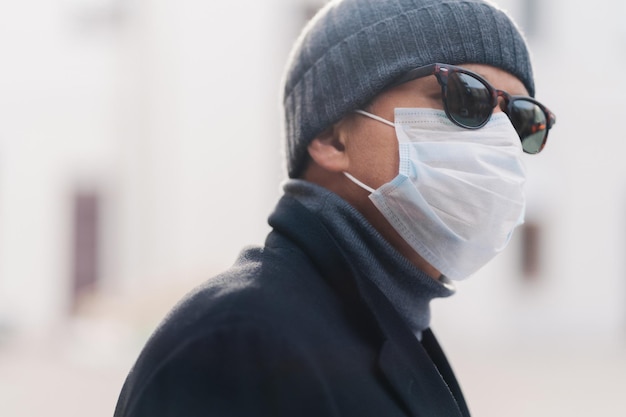 La imagen de un hombre adulto usa sombras y una máscara médica protectora camina al aire libre durante la epidemia de coronavirus mira a un lado piensa cómo superar el fondo borroso del virus El hombre tiene alergia estacional