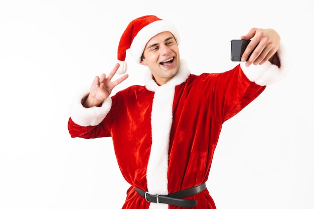 Imagen de hombre alegre de 30 años en traje de santa claus con smartphone y tomando selfie