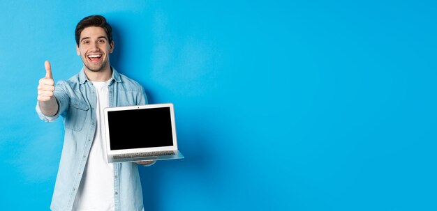 Foto imagen de un hombre apuesto satisfecho que muestra el pulgar hacia arriba de la pantalla del portátil en señal de aprobación como sitio web o internet