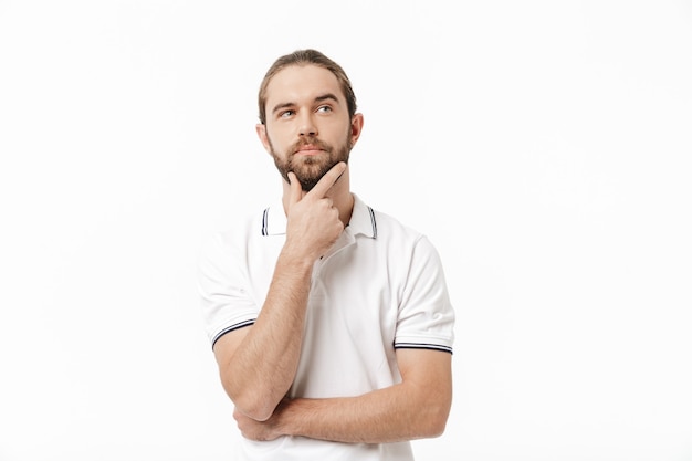 Imagen de un hombre barbudo guapo joven de pensamiento concentrado posando aislado sobre la pared blanca.