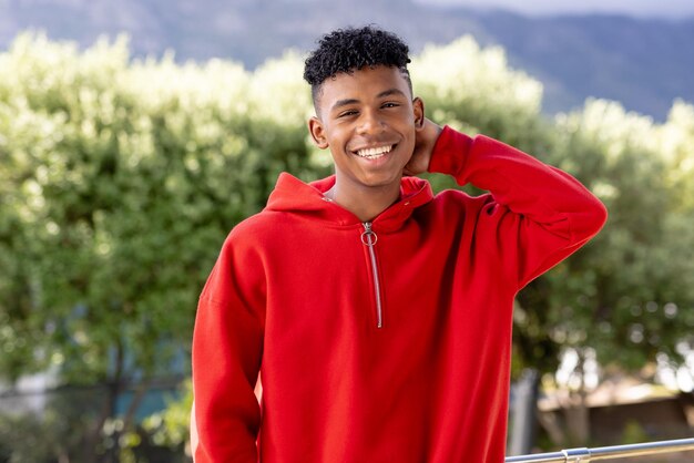 Foto imagen de un hombre birracial sonriente con una capucha roja y espacio de copia sobre árboles en el fondo. concepto de moda, ropa informal y naturaleza.