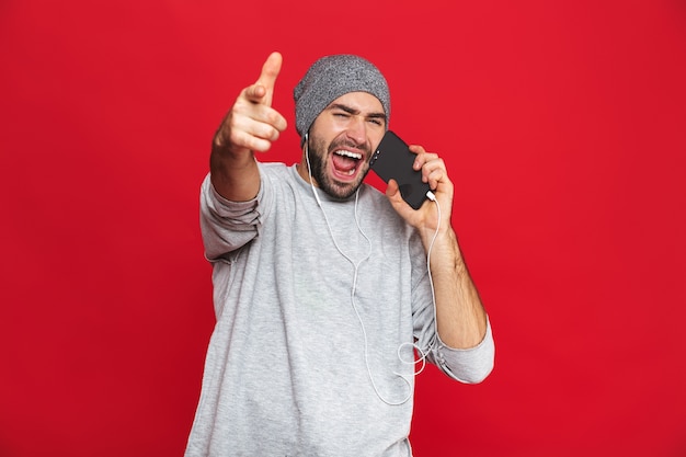 Imagen de hombre emocional de 30 años con auriculares sosteniendo teléfono celular y cantando aislado