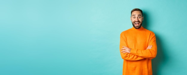 Foto imagen de un hombre feliz y sorprendido reaccionando a las noticias mirando asombrado de pie en un suéter naranja contra