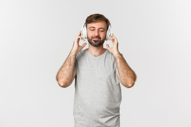Imagen de hombre guapo con barba en camiseta gris, ojos cerrados y sonriendo con satisfacción de la música