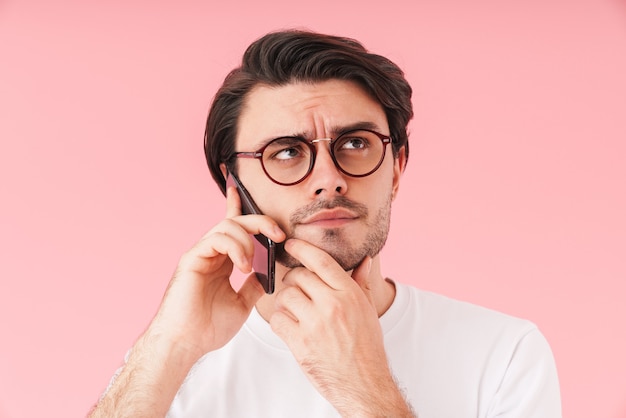 Imagen de hombre guapo desconcertado con anteojos hablando por teléfono celular y pensando aislado